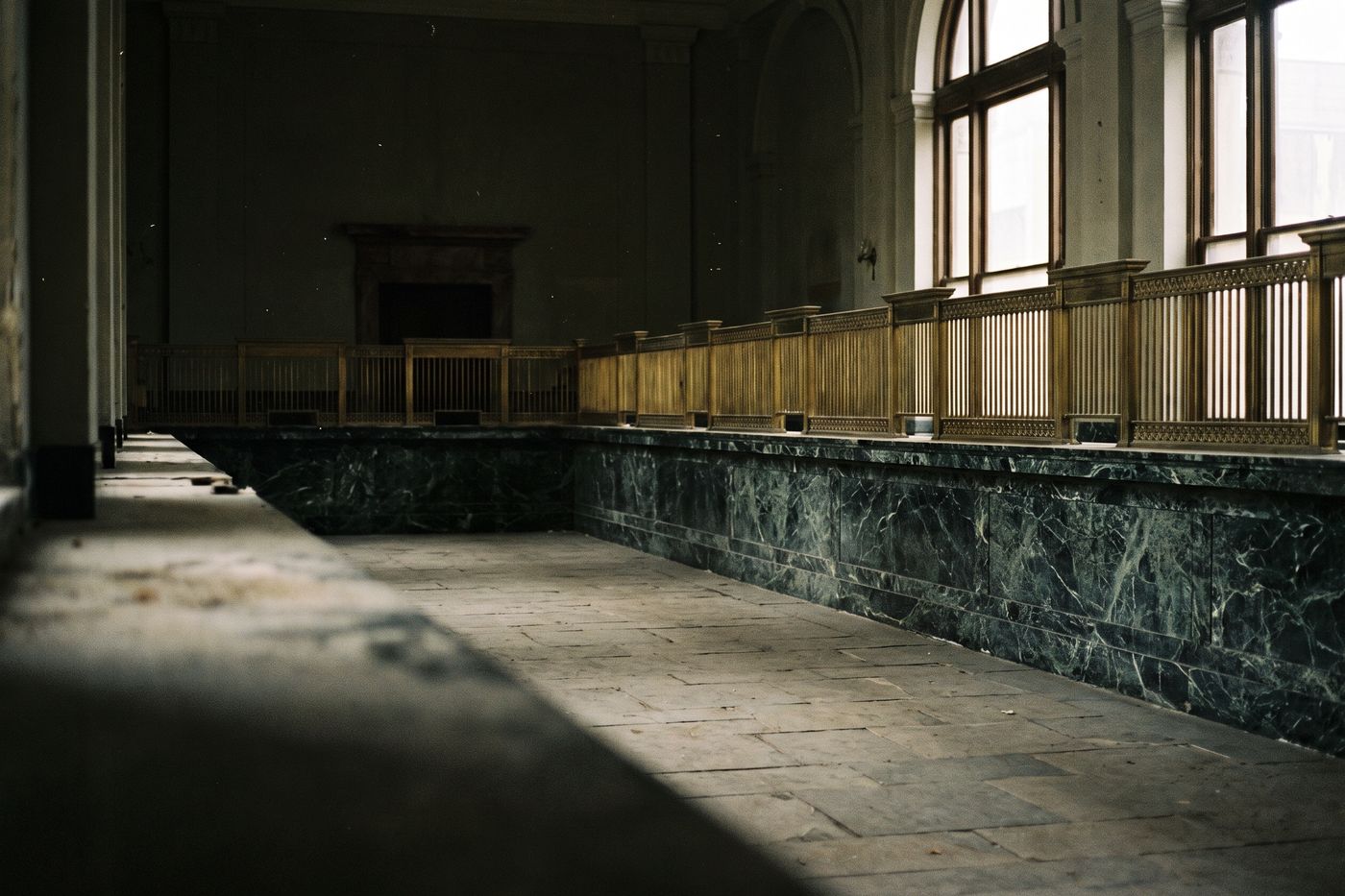 An empty old bank counter of green-veined marble with brass teller grilles, no one present