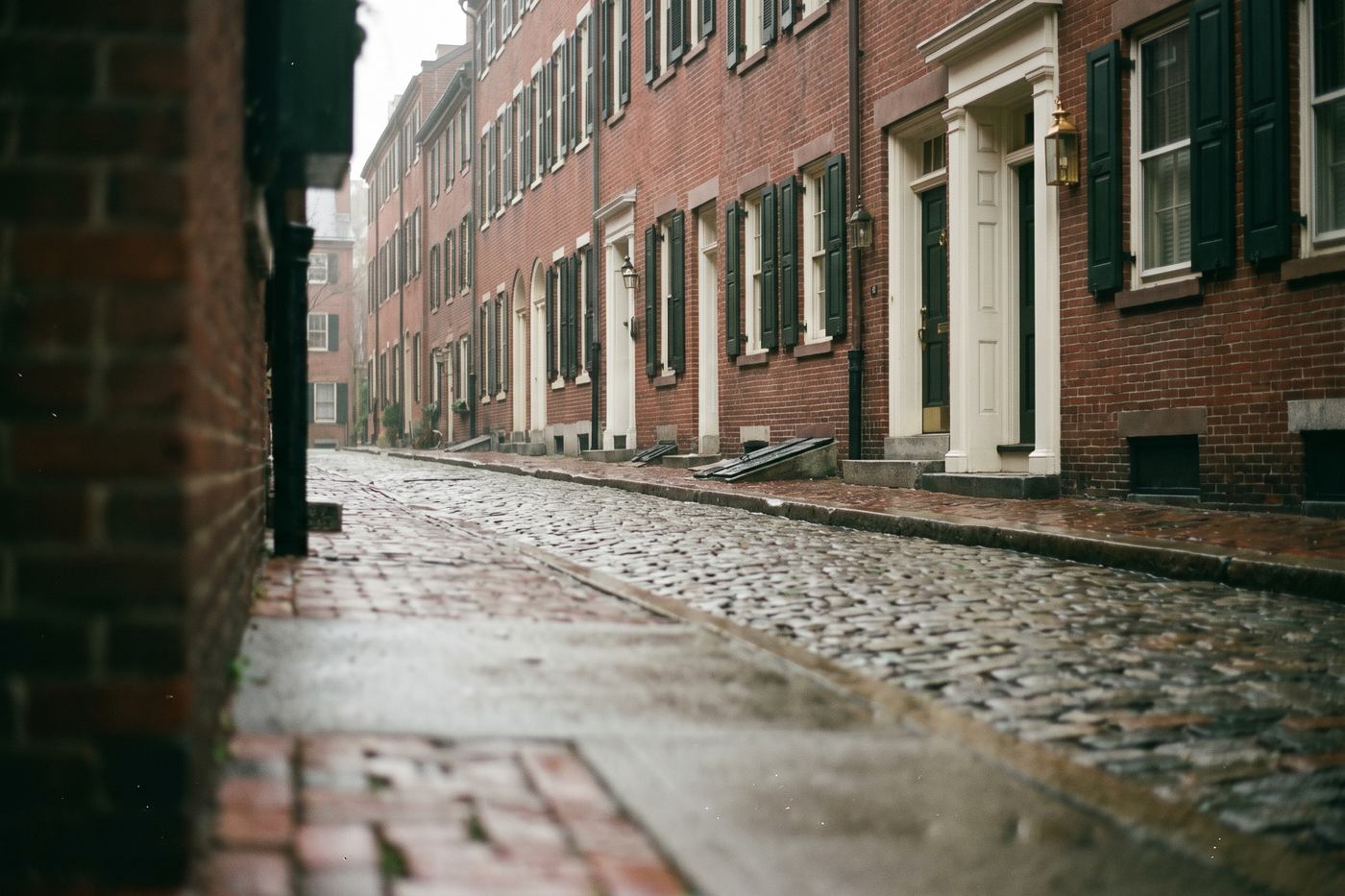 A quiet brick street of old colonial row houses with dark green shutters in soft morning light