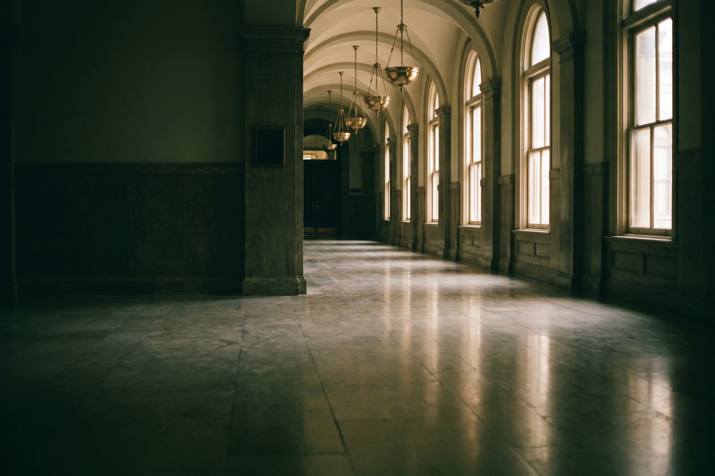 A long marble corridor inside an old state capitol with tall windows and brass light fixtures, empty