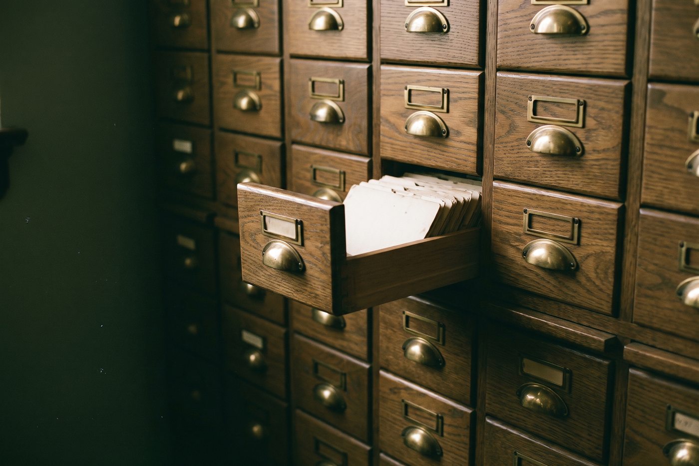 Rows of small oak card catalog drawers with brass pulls and empty brass label holders