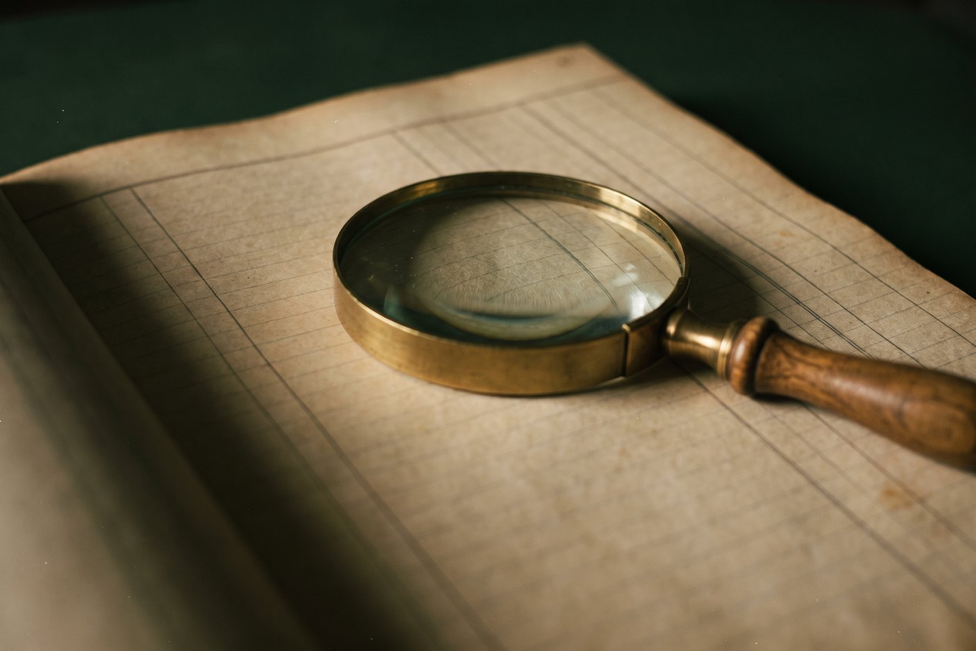 A brass-rimmed magnifying glass resting on the ruled columns of an old ledger page
