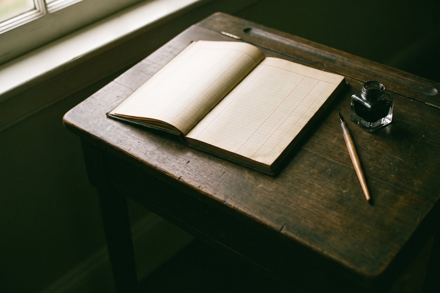 A narrow stock transfer ledger lying open with blank ruled columns, a dip pen and a glass inkwell beside it