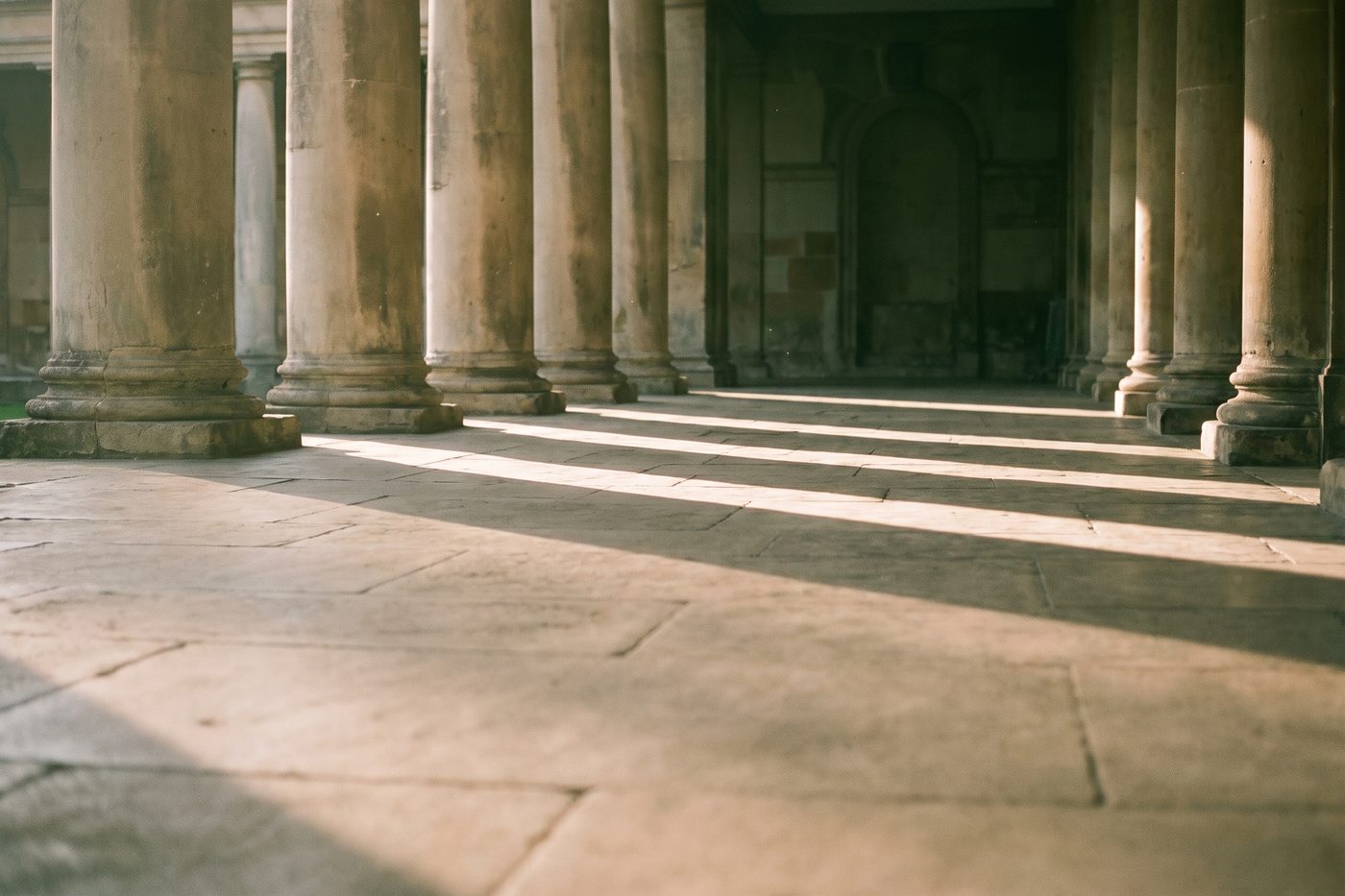 Tall stone columns casting long parallel shadows along an empty colonnade